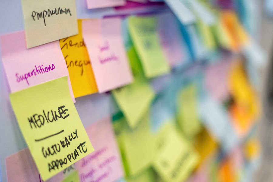 A close view of pastel sticky notes on a board, superstitions, empowerment and culturally appropriate medicine in focus and the rest falling away into colour.