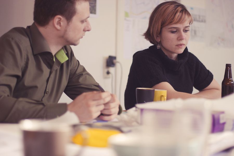 Two people sit at a table looking down at the papers between them, coffee cups in the foreground and the room thrown out of focus behind.