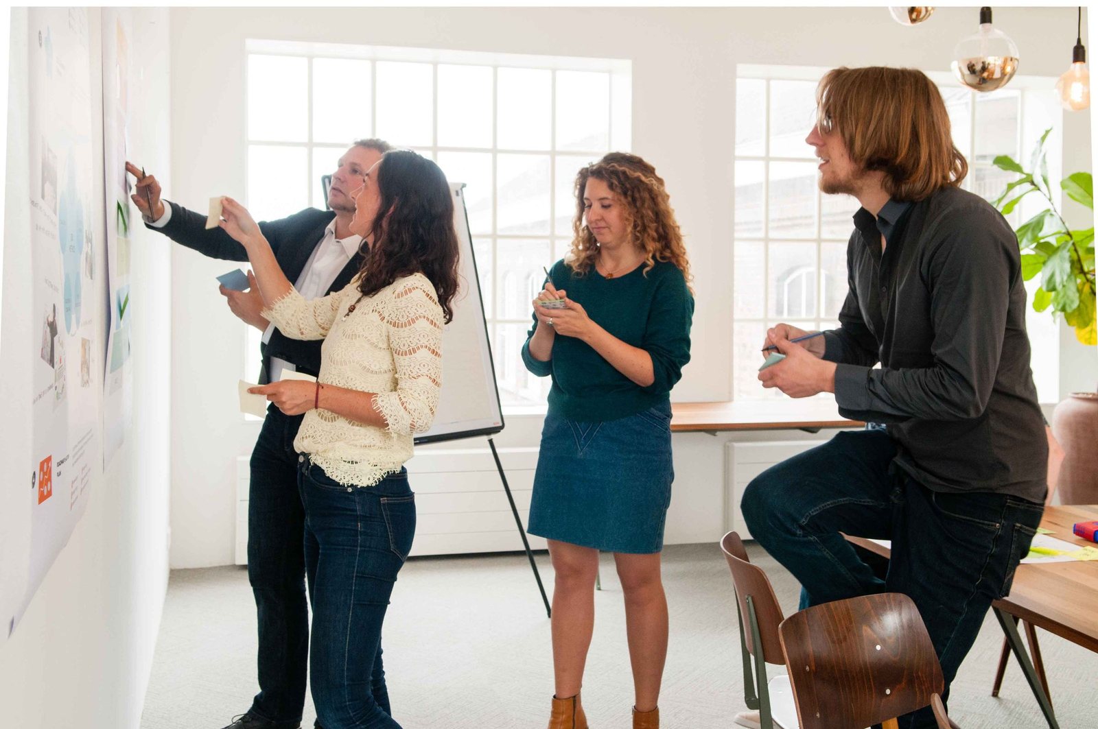 Three people work at a whiteboard by a tall window, drawing and talking at the same time.
