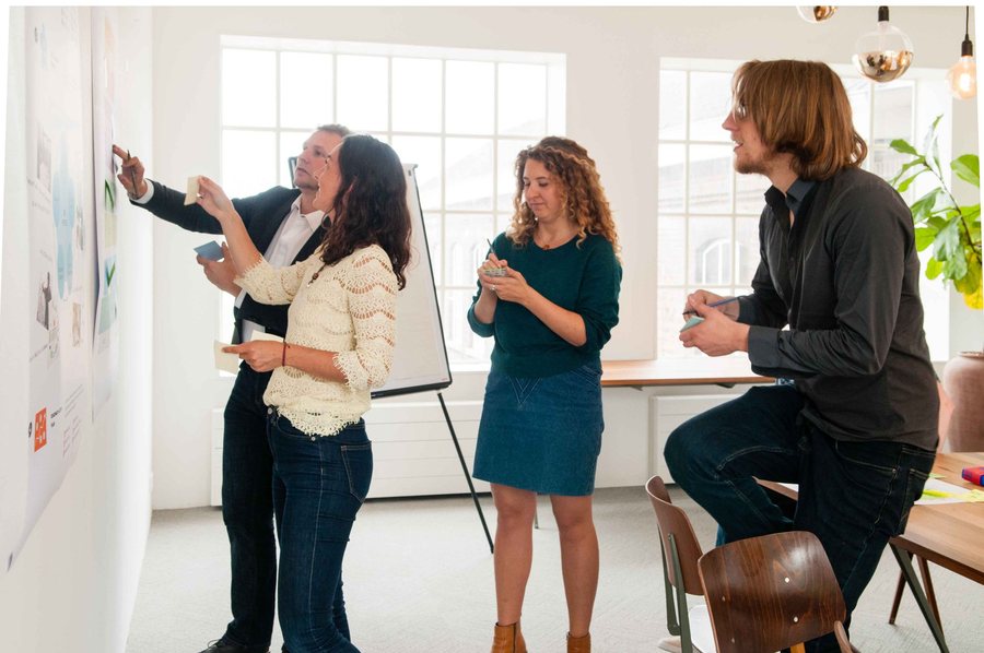 Four people stand at a studio wall placing cards on it, talking through where each one goes, a flip chart beside them.